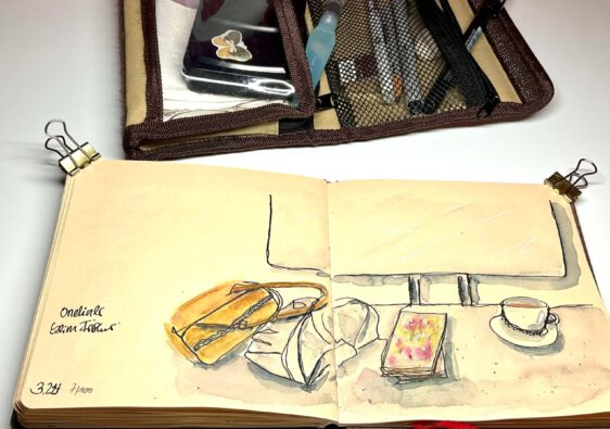 das Bild zeigt ein aufgeschlagenes Künstlerskizzenbuch, in dem ein eine Szene beim Friseur gemalt wurde (Spiegel, Ablage mit Kaffeetasse, Handtasche und Manga)