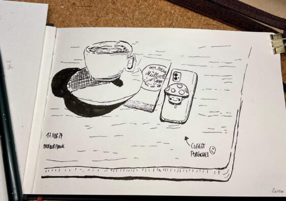Ein aufgeschlagenes Skizzenbuch mit einer schwarz/weiß Zeichnung einer Kaffeetasse und eines Handys