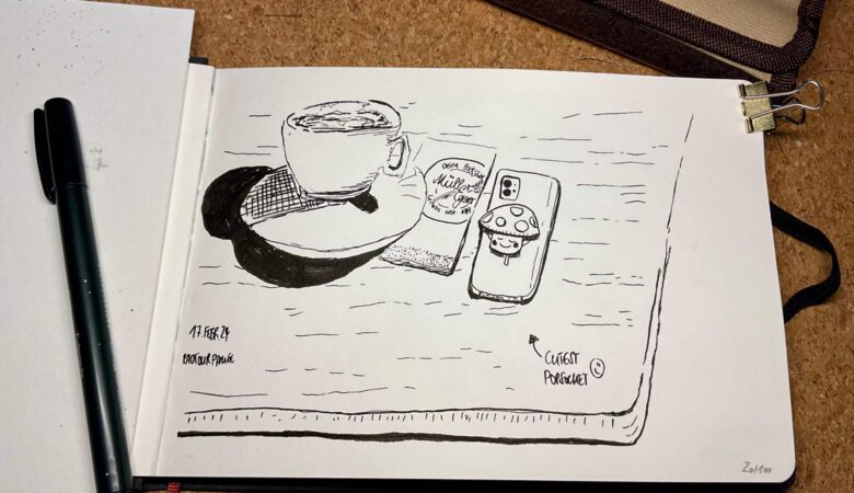 Ein aufgeschlagenes Skizzenbuch mit einer schwarz/weiß Zeichnung einer Kaffeetasse und eines Handys